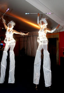 two led light stiltwalkers in white holding a baton